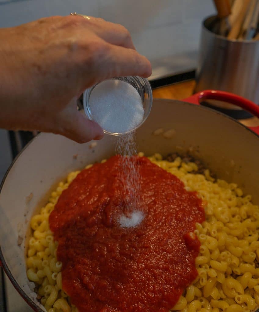 adding sugar to noodles and tomato sauce in dutch oven