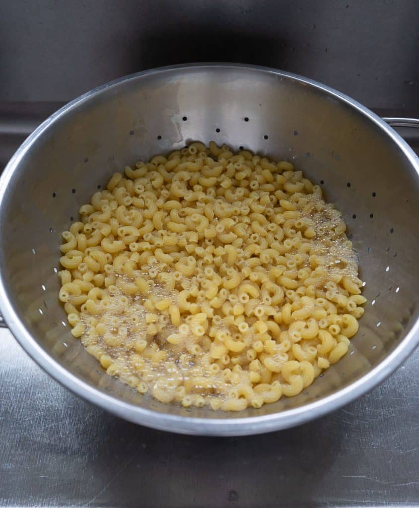 boiled and drained macaroni noodles in a colander in kitchen sink