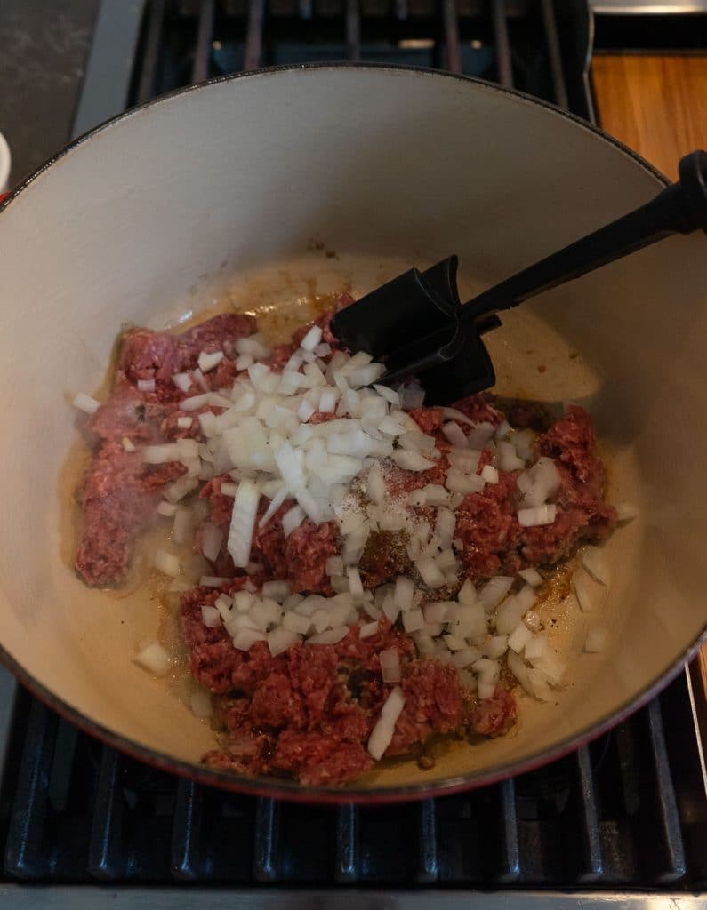 ground beef, seasonings, and chopped onion in the bottom of dutch oven on stovetop
