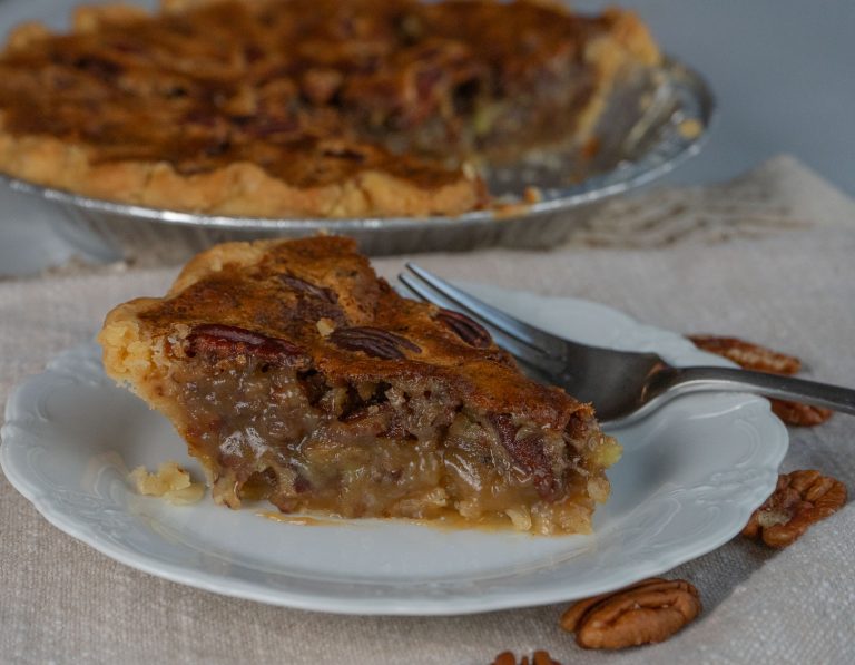 slice of pecan pie on a white plate with a whole pie in the background