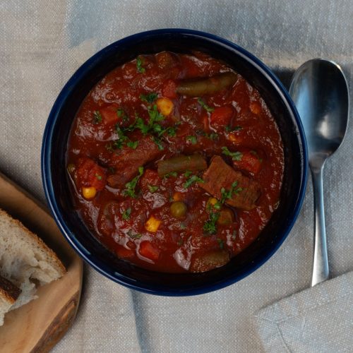 blue bowl on a tan table with a napkin and a spoon on the right side of the bowl