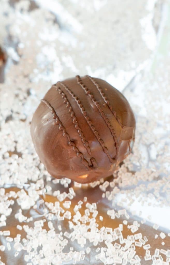 one chocolate covered peanut butter ball on a silver surface covered in sparkle sugar