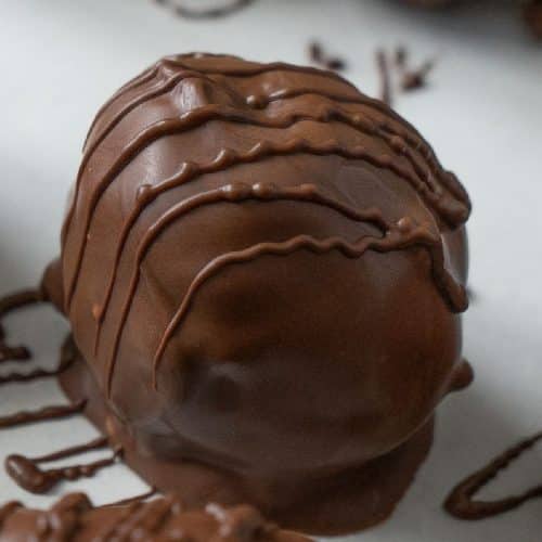 chocolate covered peanut butter ball on chocolate drizzled parchment paper