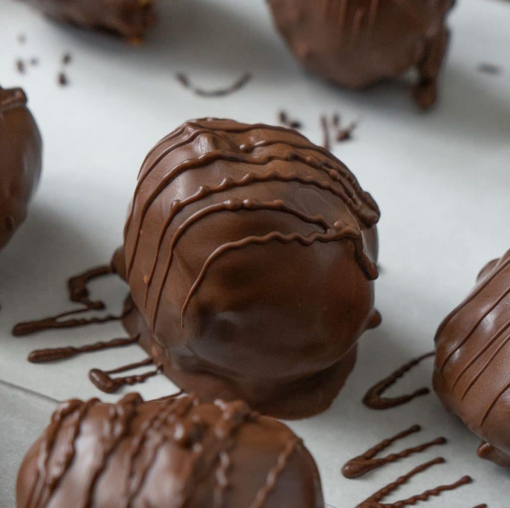 chocolate covered peanut butter ball on white parchment drizzled with chocolate