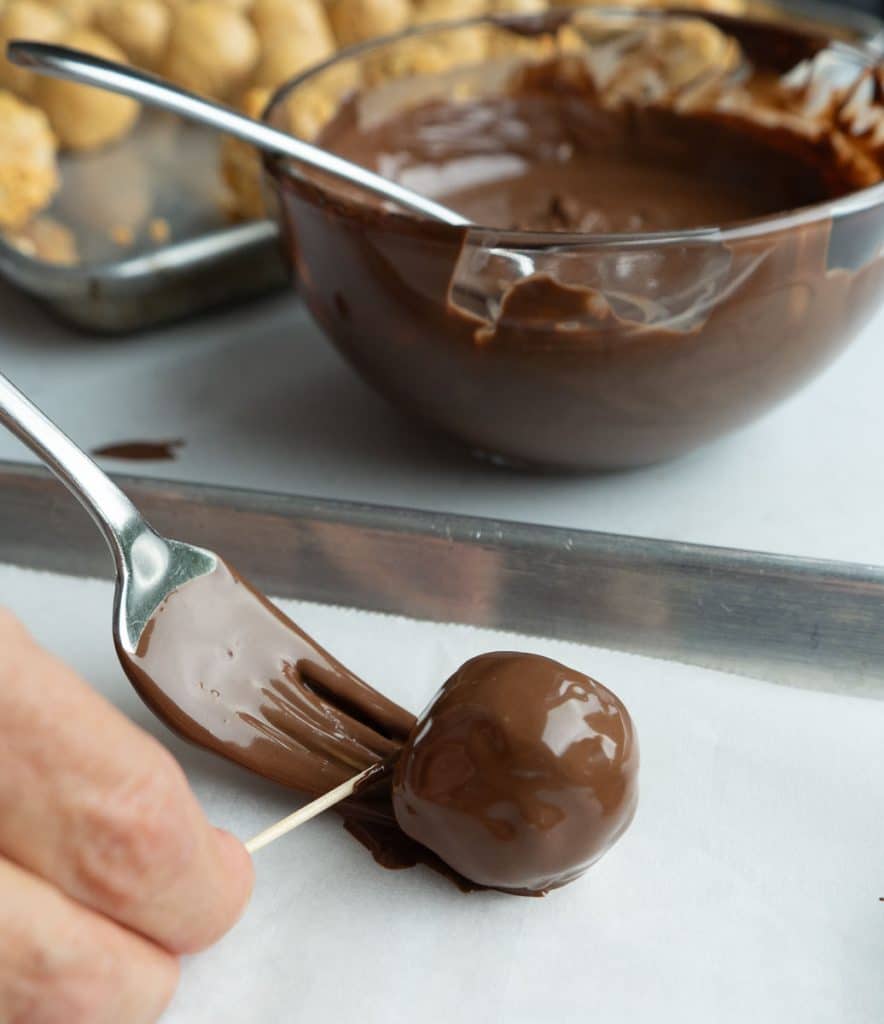 DSCN5968 setting chocolate dipped peanut butter ball on a parchment lined baking sheet with hand using a toothpick to push ball off the fork