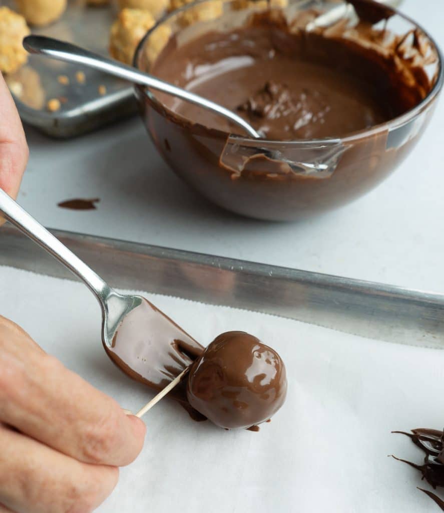 setting chocolate dipped peanut butter ball on a parchment lined baking sheet with hand using a toothpick to push ball off the fork
