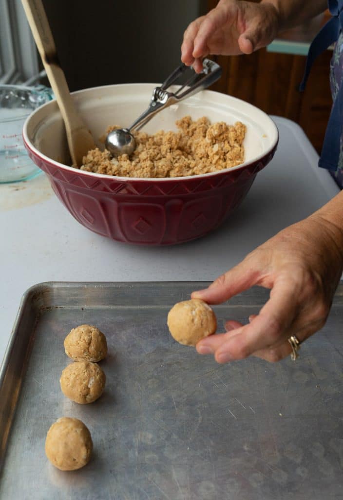pb2collage hand placing rolled peanut butter ball on a baking sheet the bowl of peanut butter with a hand scooping out the peanut butter filling with a cookie scoop