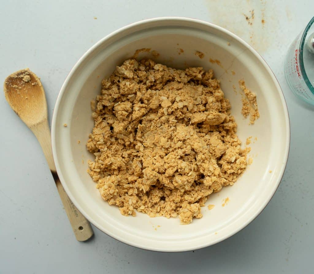 peanut butter ball filling in a glass bowl on a gray countertop with a wooden spoon to the left of the bowl