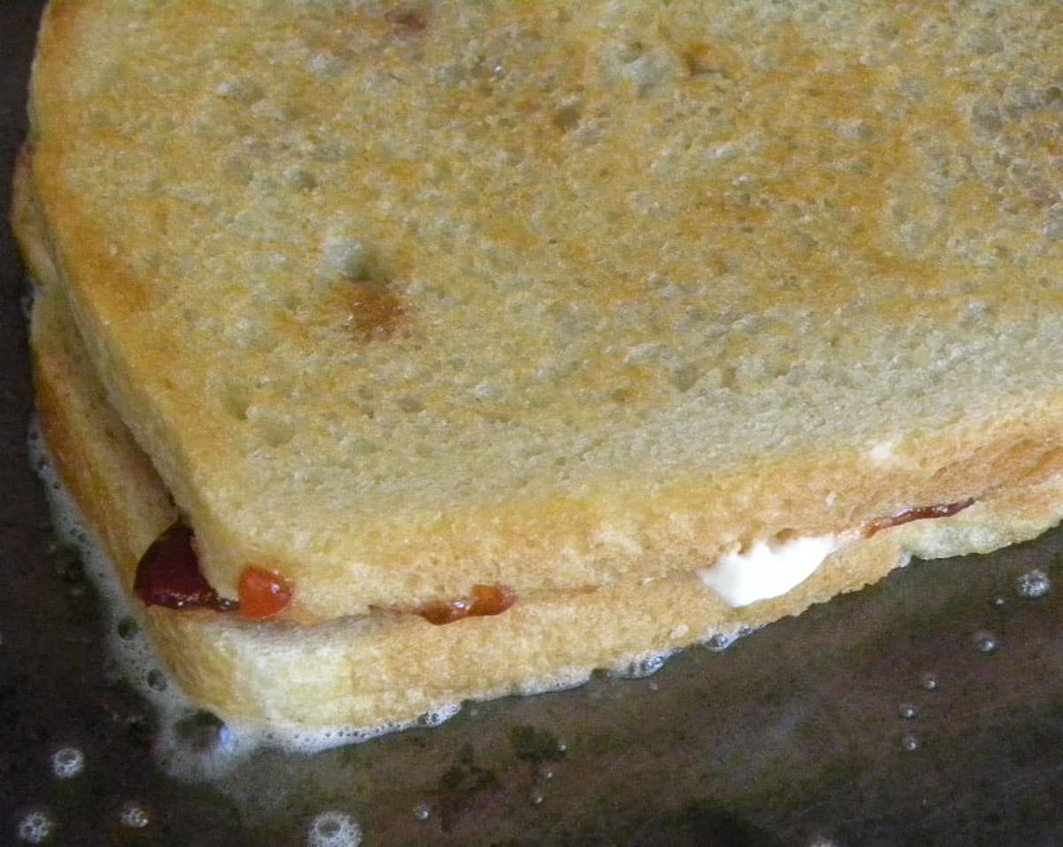 Two slices of white bread with goat cheese and jam being grilled on a griddle