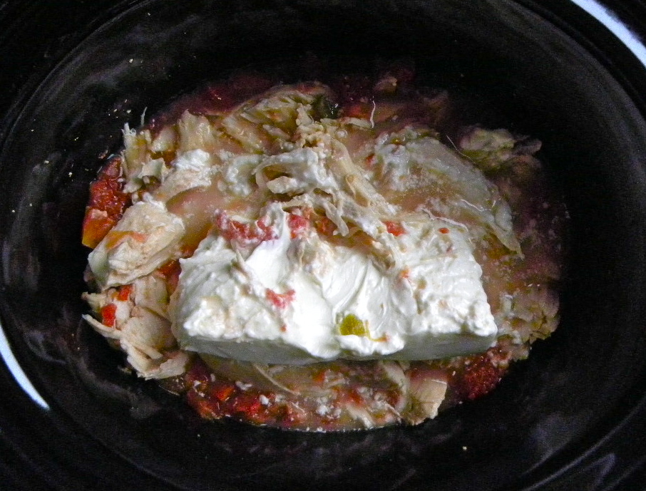 chunk of cream cheese in a crock pot full of chicken and diced tomato