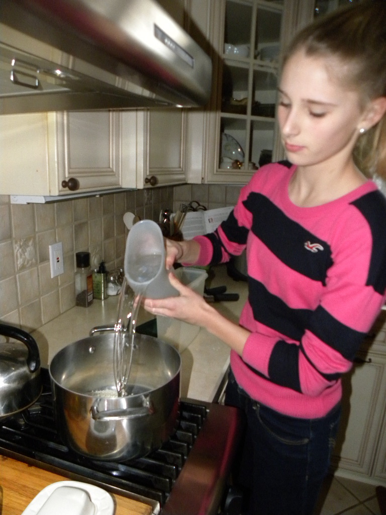 girl pouring water into large pot on stove