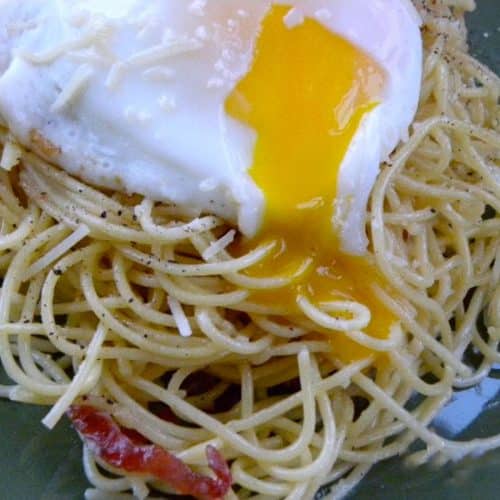 plate with spaghetti noodles and an egg on top pasta carbonara on a green plate