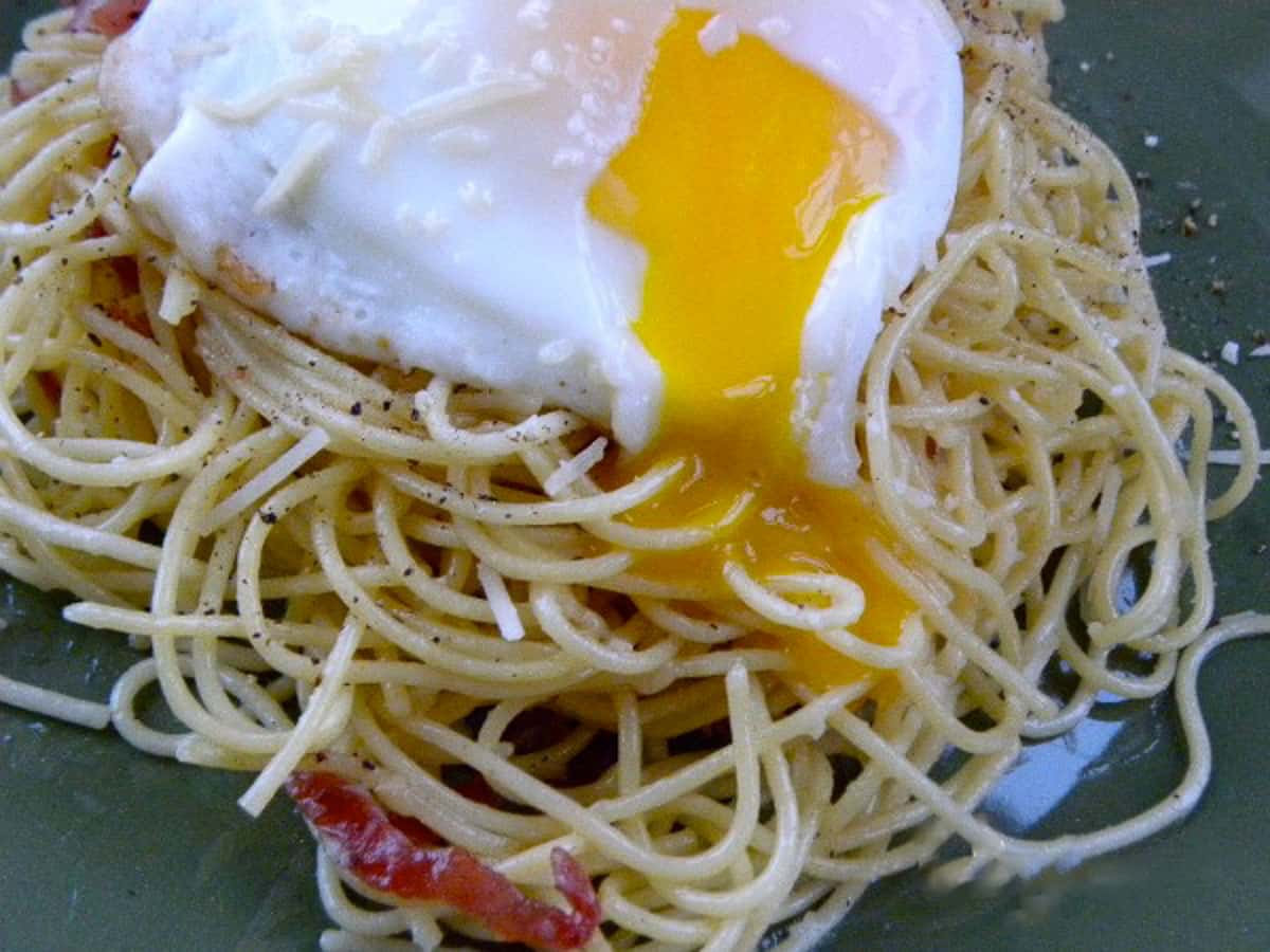 plate with spaghetti noodles and an egg on top pasta carbonara on a green plate