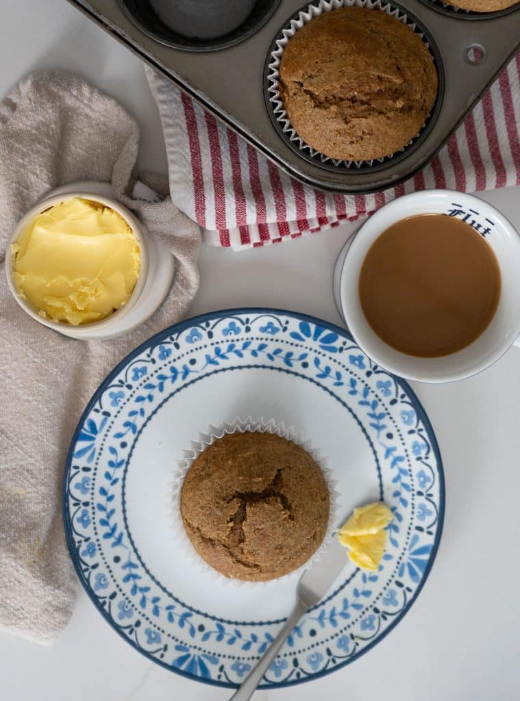 top photo has muffin tin with baked muffins in it, a crock  of butter, a cup of coffee and then a whole bran muffin is sitting on a white plate with blue flowers around the edge with a butter knife with butter on it laying beside the muffin