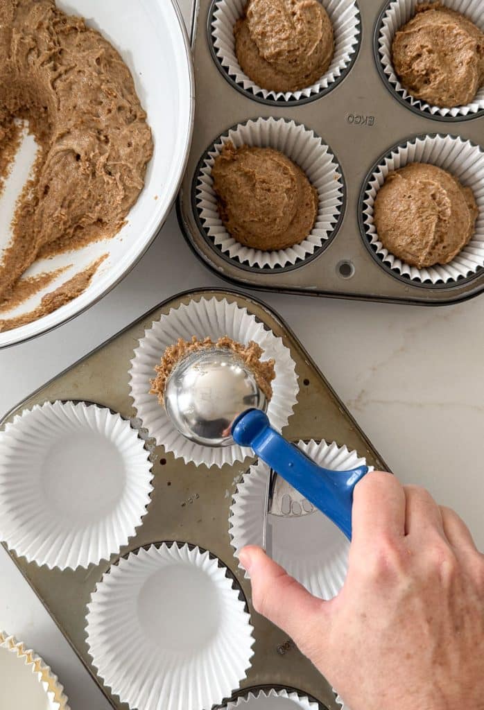 filling muffin tins with bran muffin batter. hand is putting batter in muffin paper with a large cookie  scoop