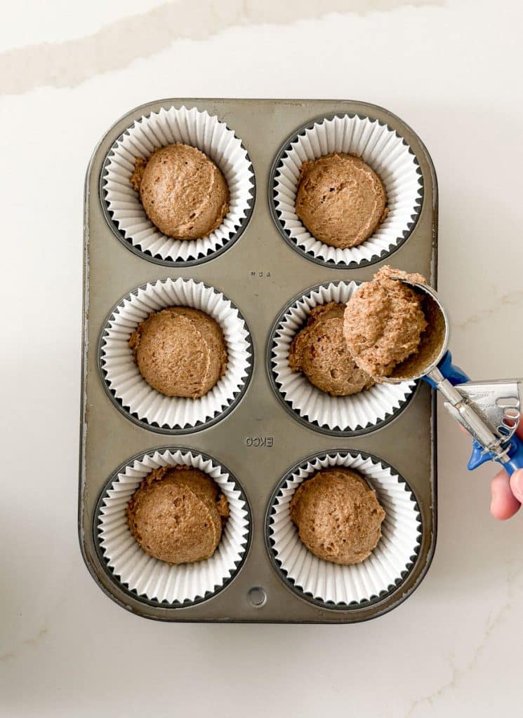 muffin tin with a cookie scoop of bran muffin batter in the middle right side of the photo
