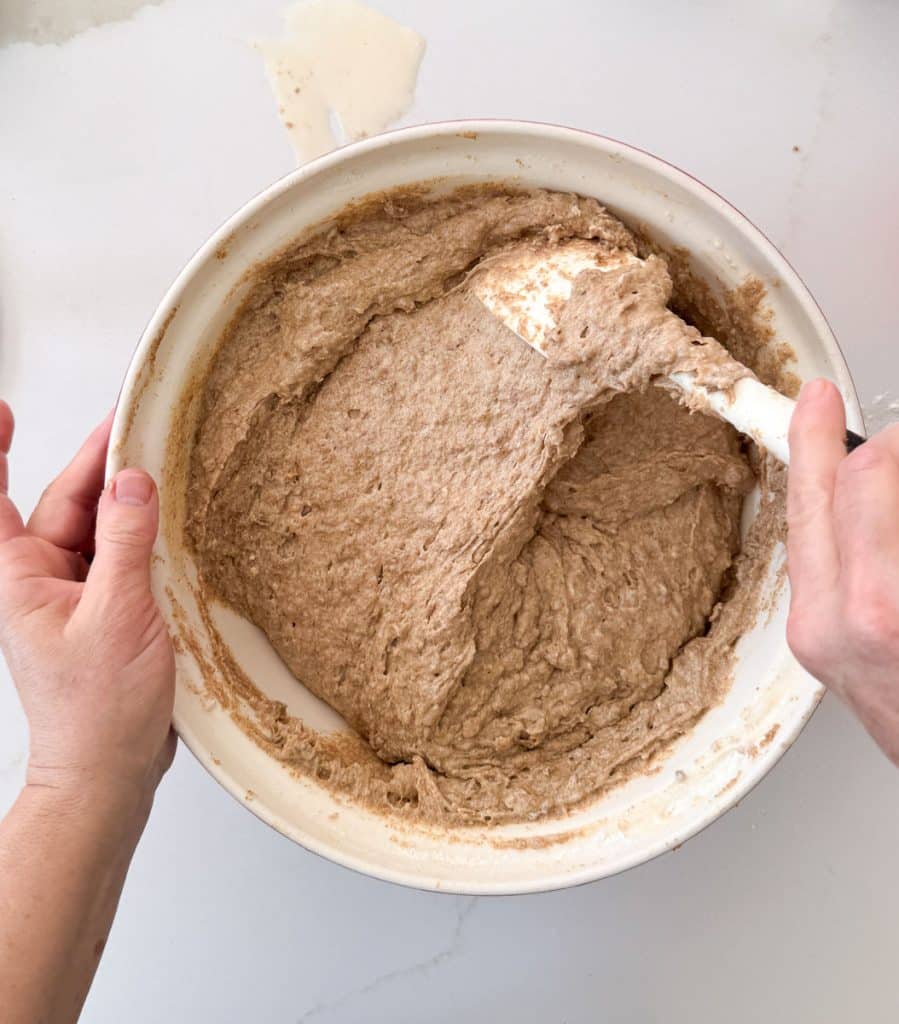 bran muffin batter being mixed in a large bowl on a white countertop 