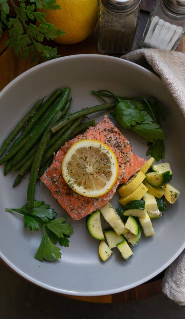 top view of baked salmon with a slice of lemon on top surrounded by vegetables on a gray plate