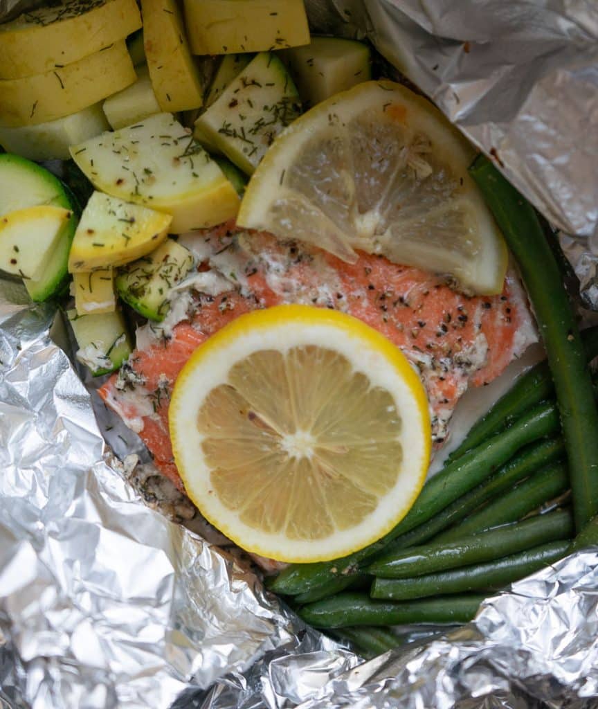 baked and opened foil packet of baked salmon with zuchini and summer squash chunks and green beans.