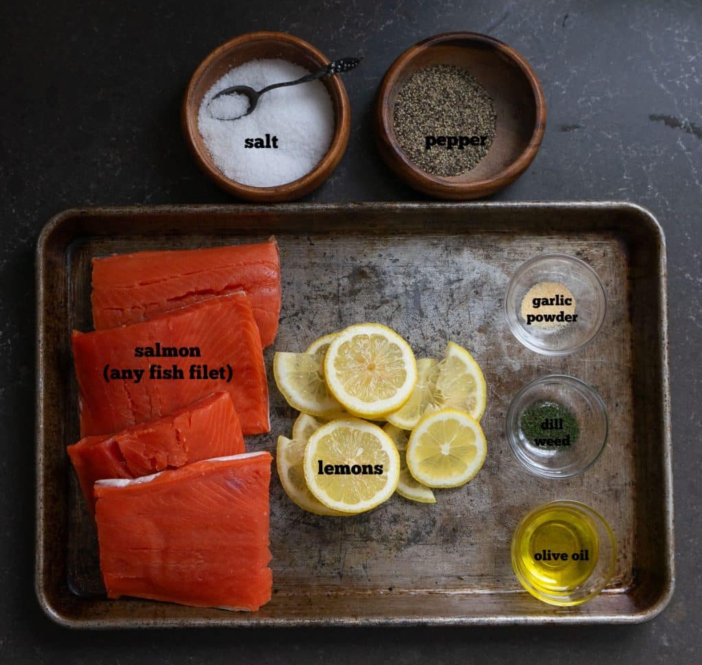 DSCN6710 ingredients for fish packets on a baking sheet that is sitting on a black counter top there are two wood bowls next to baking sheet with salt and pepper in them