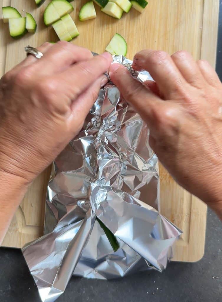 DSCN4598 folding aluminum foil into a pouch around the fish and vegetables on a wood cutting board