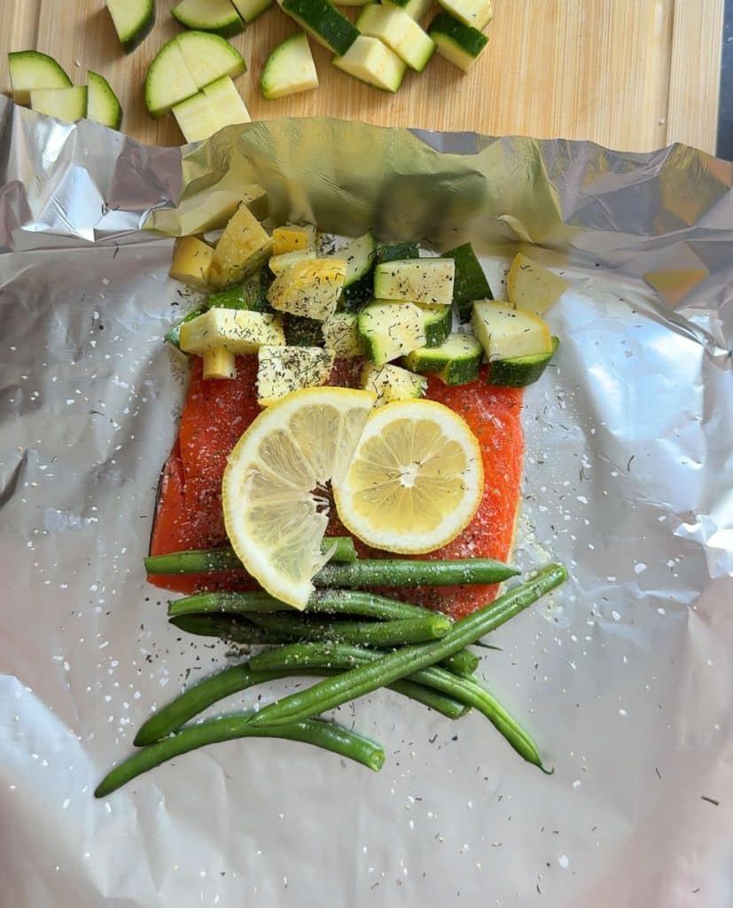 DSCN6713 salmon fillet surrounded by vegetables and topped with fresh lemon slices on aluminum foil