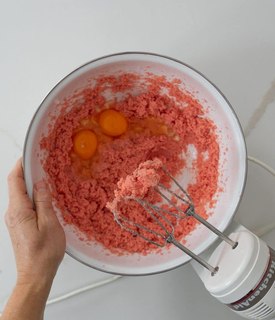 adding eggs to the bowl hand mixer is in the lower right corner a hand is on the left side of the bowl