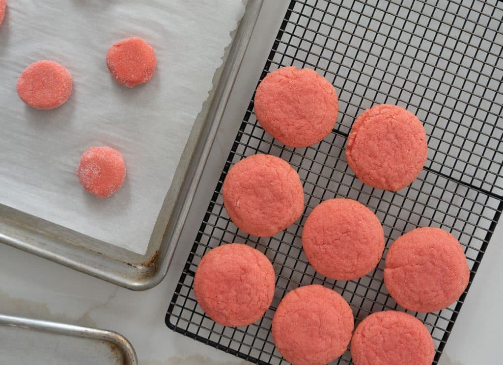 cookies on a cooling rack cooling and cookie dough balls on a baking sheet ready to go in the oven 