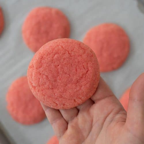 hand holding a jello sugar cookie over a baking sheet of baked cookies
