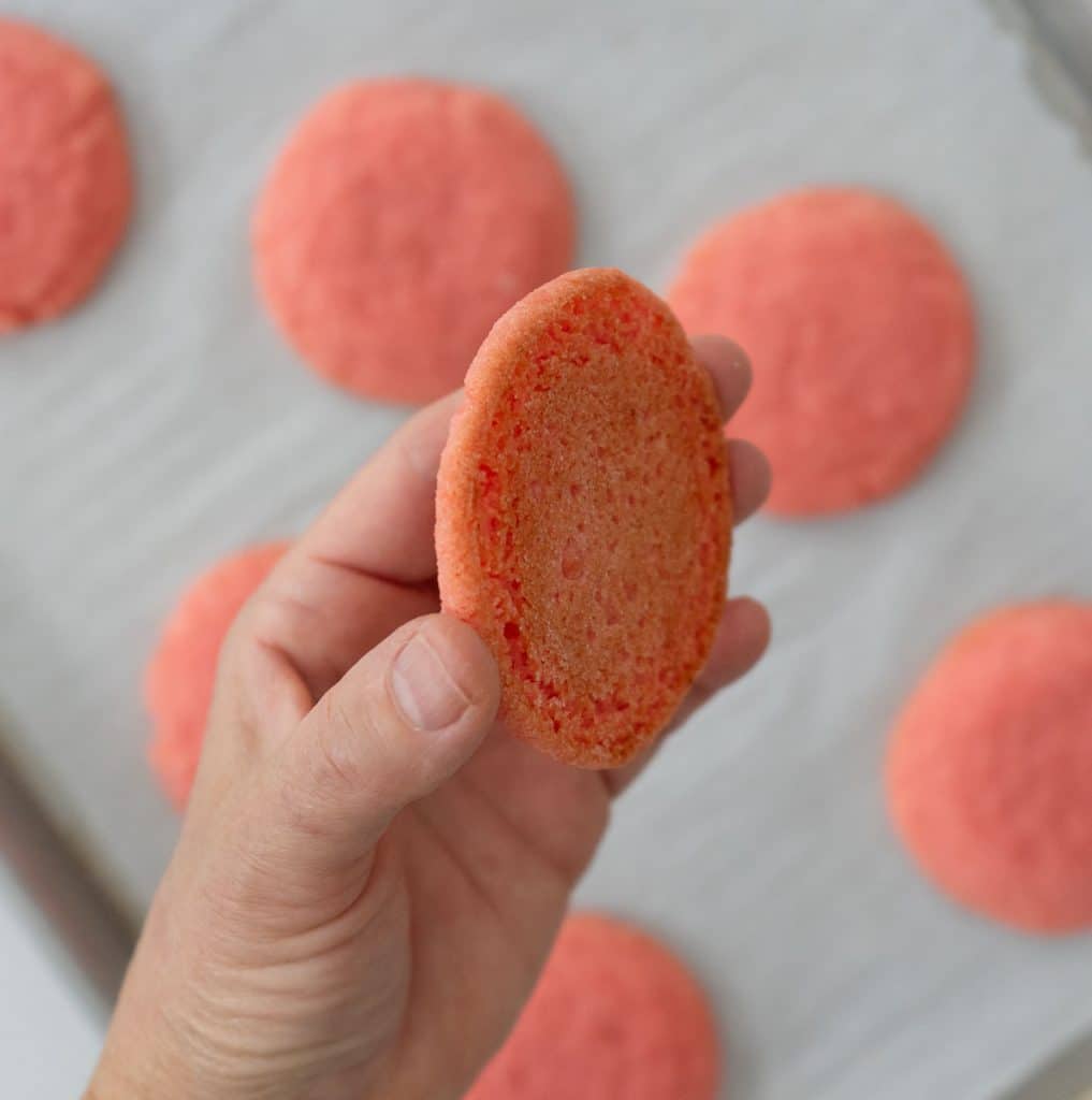 hand holding a baked cookie over a pan of baked cookies showing the bottom of the cookie