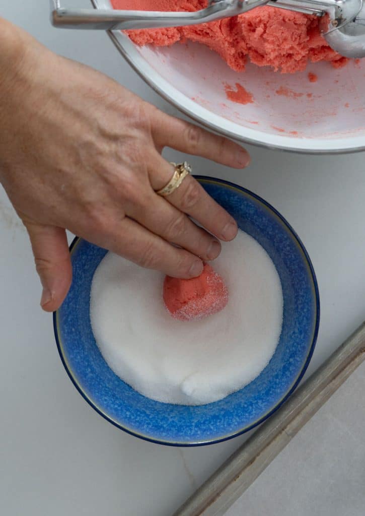 rolling cookie dough ball in a bowl of sugar