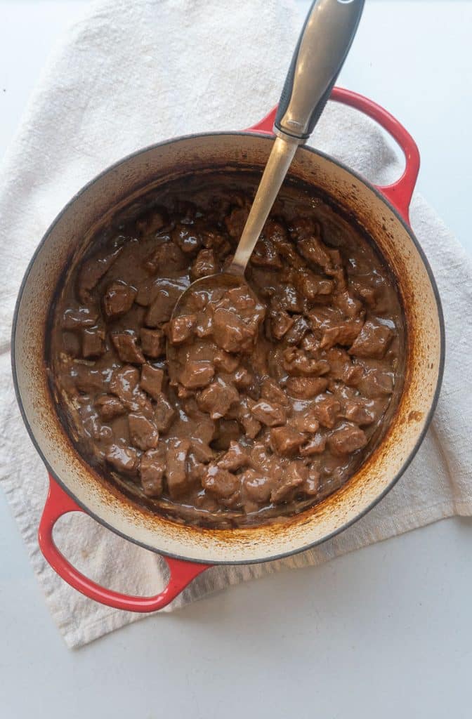 pot of no peek beef tips with a spoon sticking out of the pot handle pointing toward the upper right corner