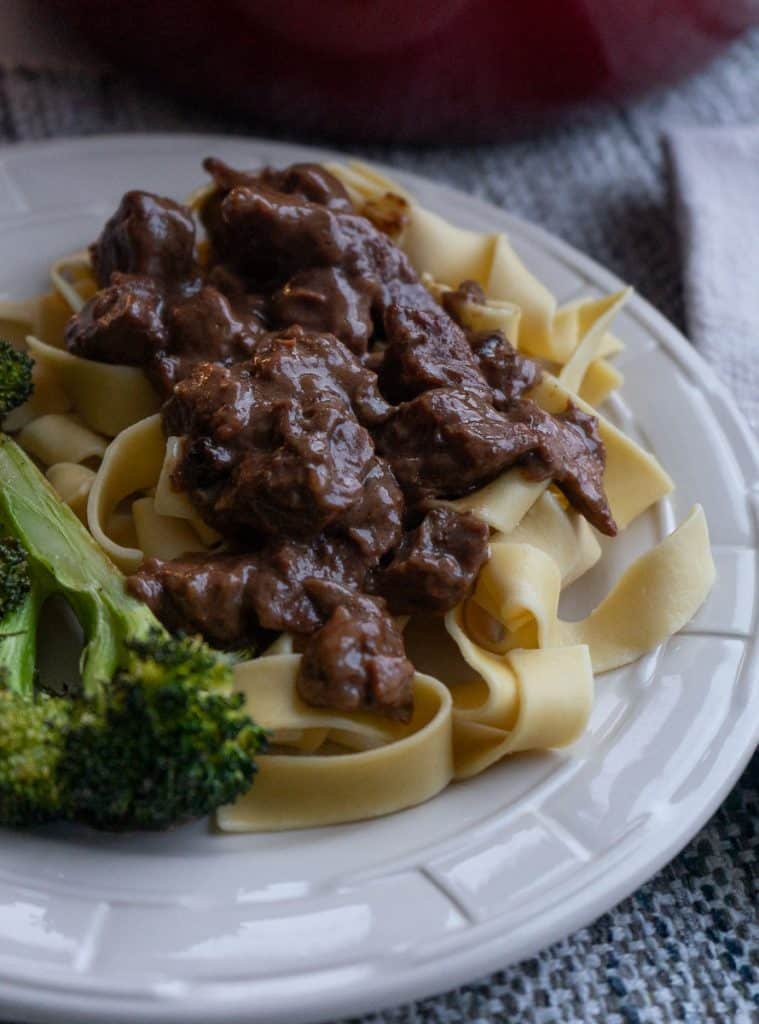 plate of no peek beef tips on a bed of egg noodles with broccoli on the side