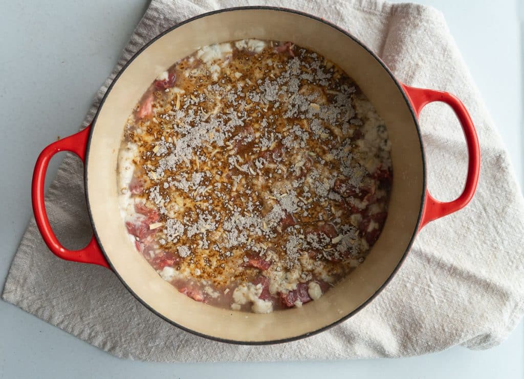 ingredients for no peek beef tips layered in a red dutch oven