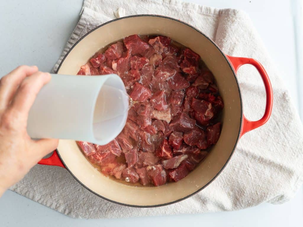 DSCN6266 pouring ginger ale over beef tips in dutch oven