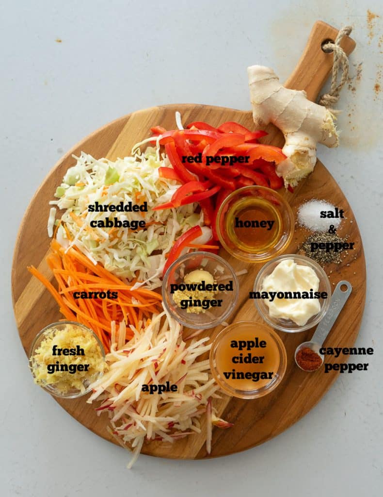 ingredients for spicy ginger slaw on a round wood cutting board that is on a white countertop