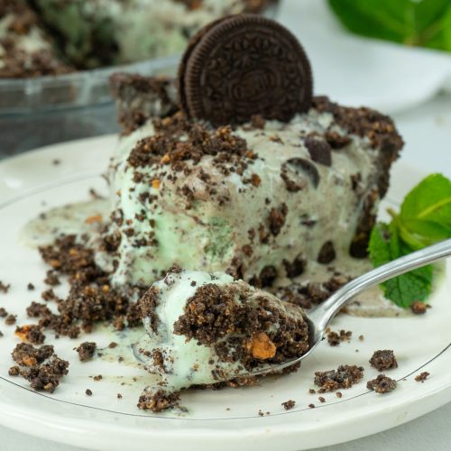 Slice of mint chocolate chip ice cream pie on a plate with whole pie in the back ground