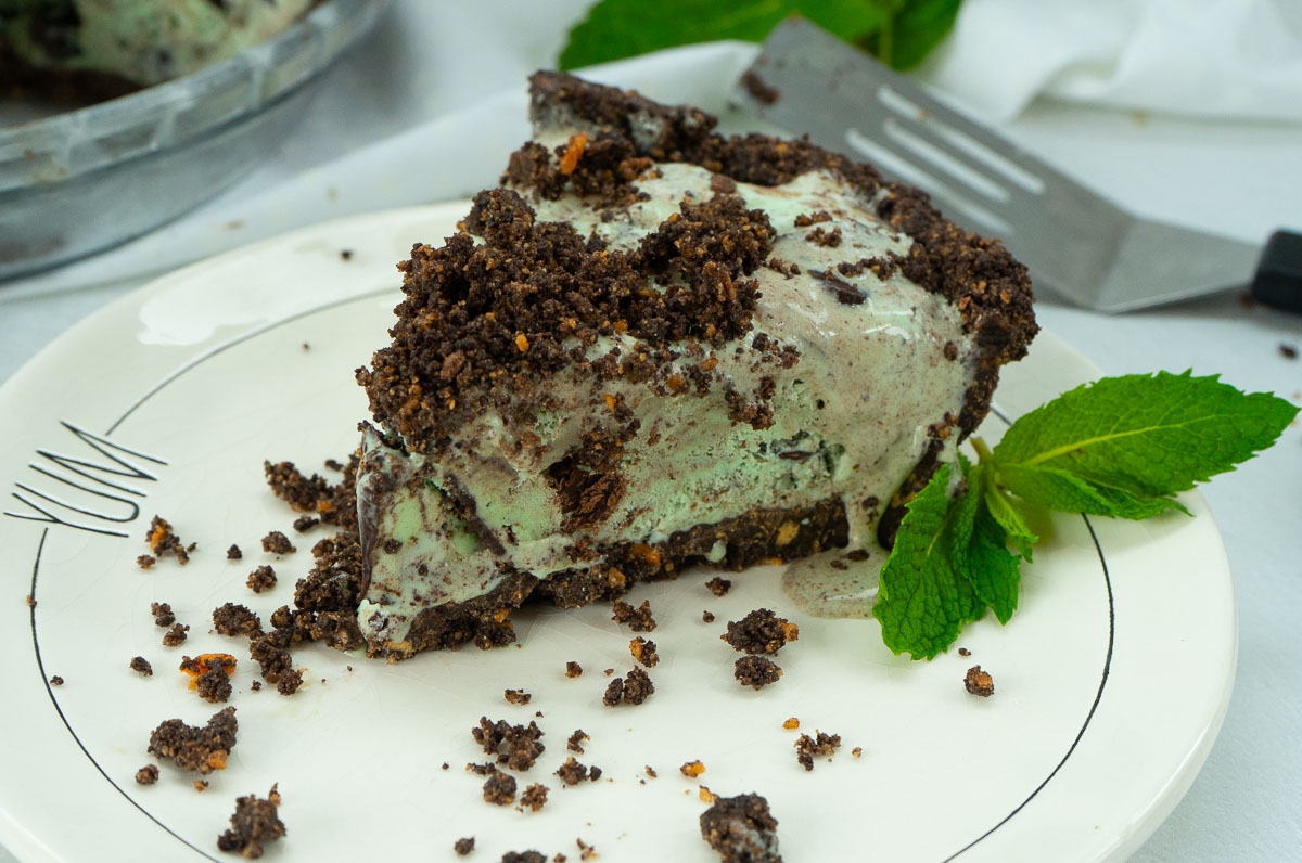 Slice of mint chocolate chip ice cream pie on a plate with whole pie in the back ground