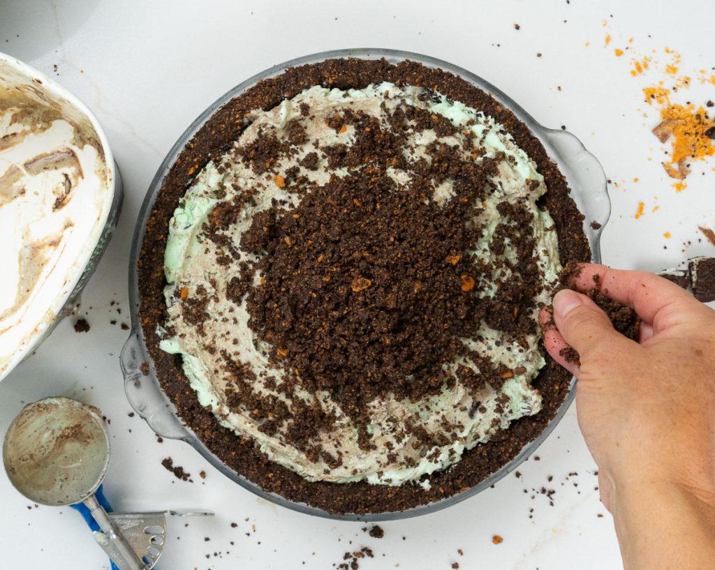 crumbling reserved cookie and candy bar crust on top of the ice cream pie