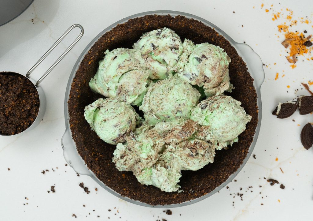 scooping mint chocolate chip ice cream into cookie crust on a white countertop