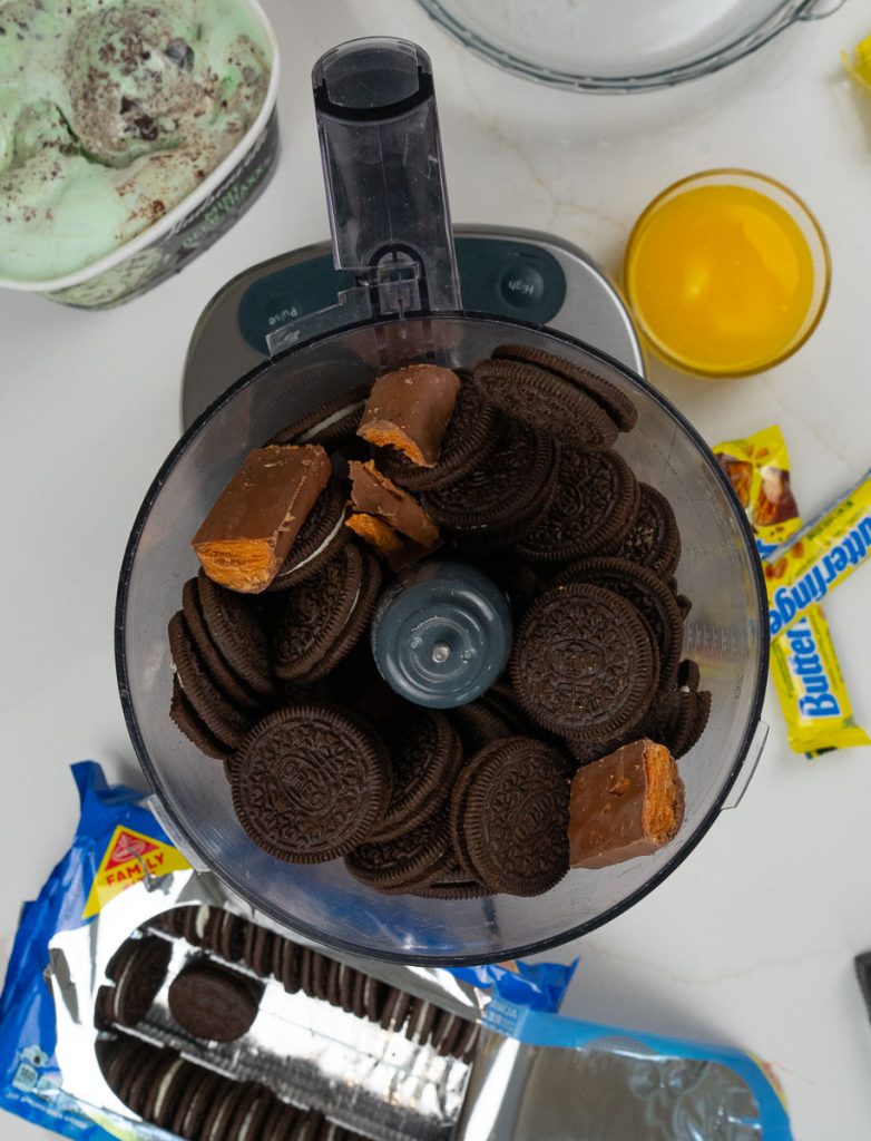 oreo cookies and butter finger bars in a food processor with a small bowl of melted butter