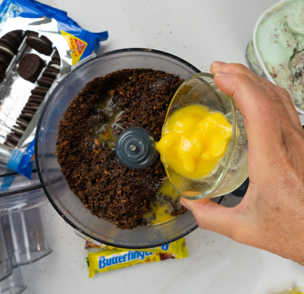 adding melted butter to cookie and candy bar crumbs in food processor