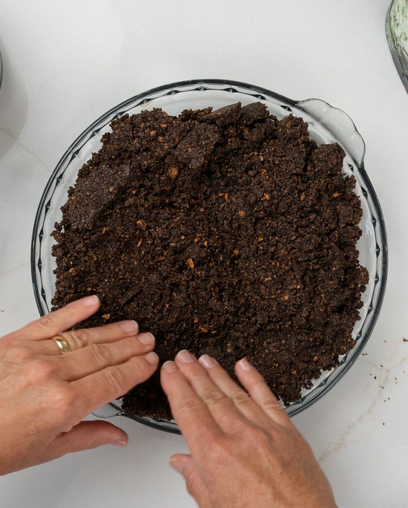 Creating the cookie crust by pressing it into the pie dish with fingers