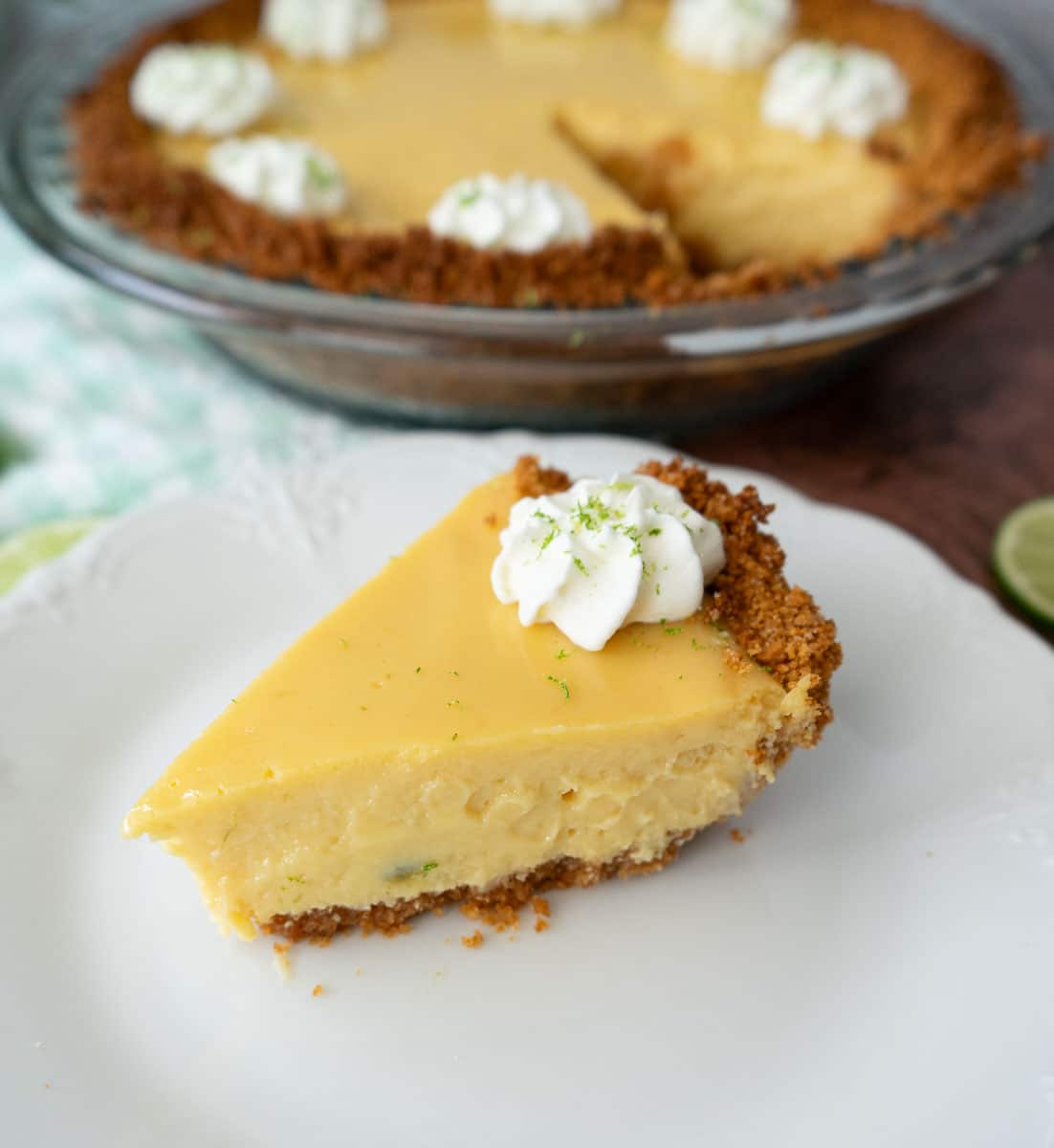 one piece of pie on a white plate with a fork on the plate the whole pie with a piece taken out is in the background of the photo