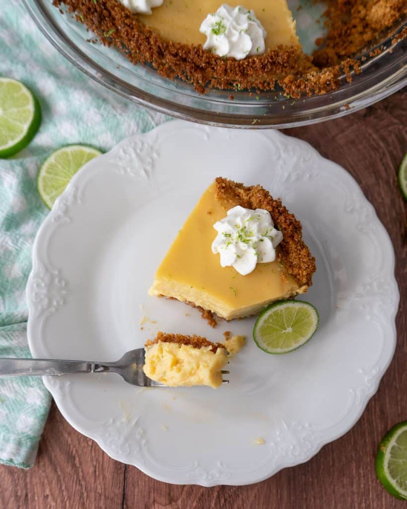 top view of one piece of key lime pie on a white plate with a fork full of pie setting on the plate the edge of whole pie is in the top of the  photo
