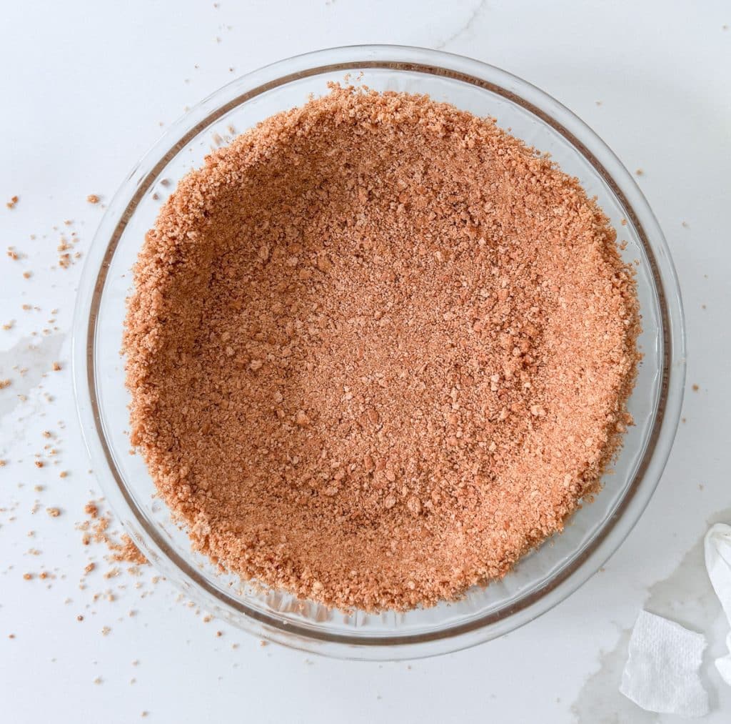 graham cracker crust on a white countertop with some graham cracker crumbs on the counter top