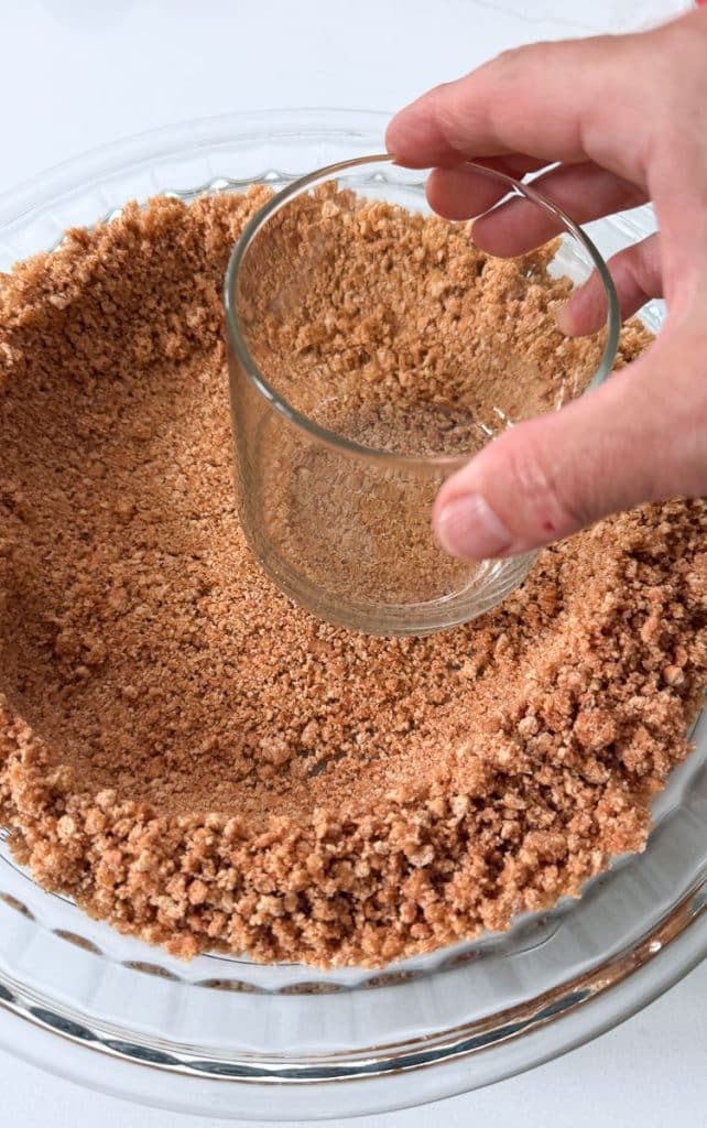 using a glass to press graham cracker crumbs into the bottom of the pie plate