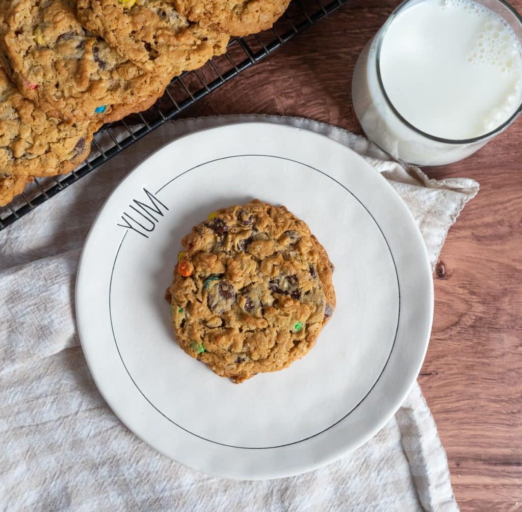 cookie on a white plate with a glass of milk next to it a cooking rach with cookies on it is in the top left corner of the photo