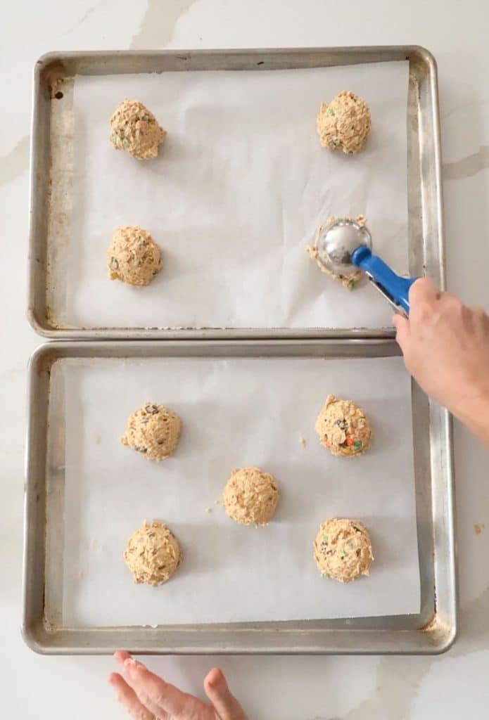 scooping out cookie dough on to baking sheets lined with parchment paper