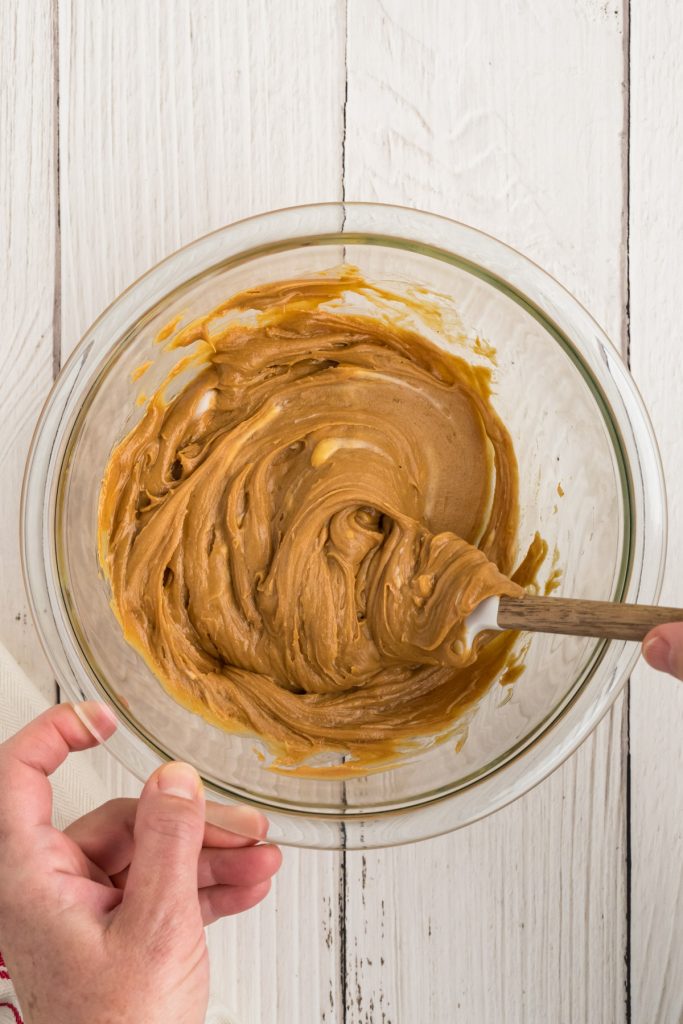 mixing peanut butter, honey, and butter together with a spatula in a clear glass bowl